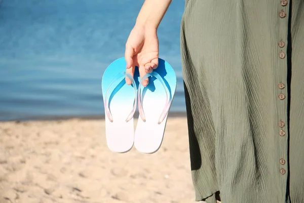 Woman holding flip-flops on beach, closeup. Space for text