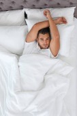 Mladý muž ležel v posteli s měkkými polštáři doma, pohled shora