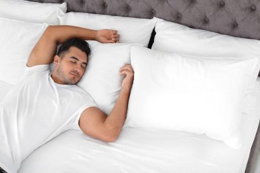 Yumuşak yastık ile evde yatakta uyuyan genç adam