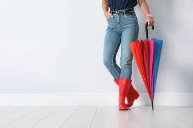 Tasarım alanı olan beyaz duvarının yakınında parlak şemsiye tutan gumboots kadında