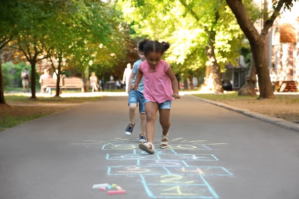 アスファルトの上にカラフルなチョークで描かれた石けり遊びを遊んでいる小さな子供たち — ストック写真