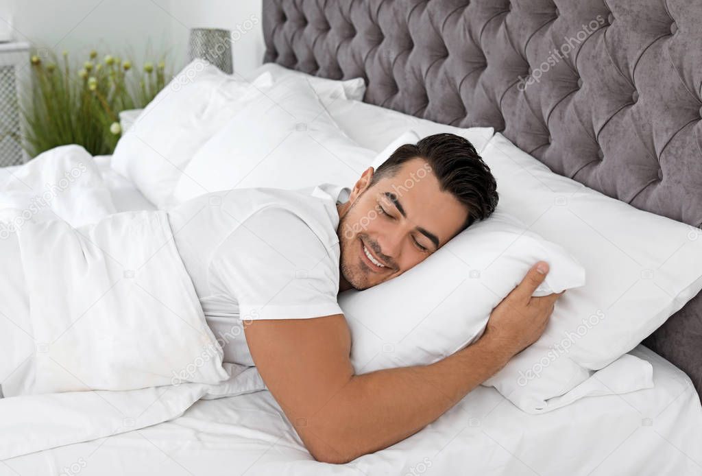 Young man sleeping in bed with soft pillows at home