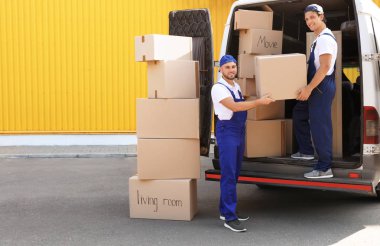Male movers unloading boxes from van outdoors clipart