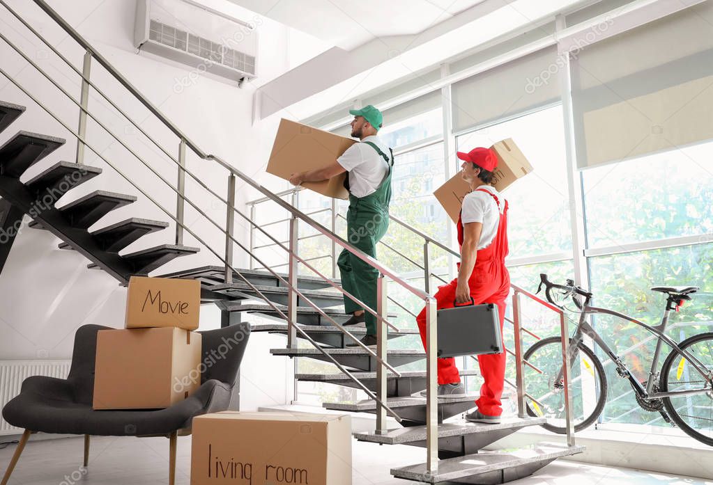 Male movers carrying boxes in new house