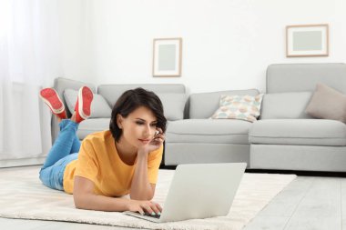 Genç kadın evde yerde yatarken modern dizüstü bilgisayar ile