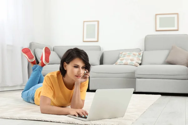 年轻妇女与现代膝上型电脑躺在地板上在家 — 图库照片