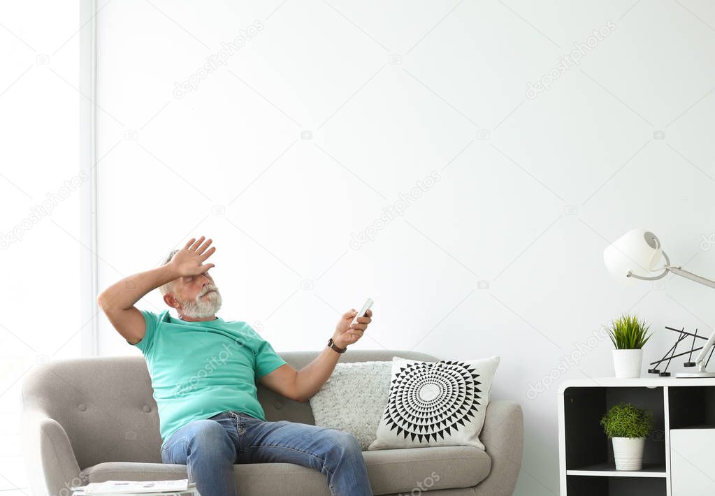 Senior man with air conditioner remote control suffering from heat at home