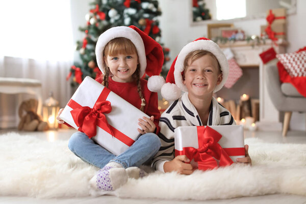 Cute little children in Santa hats with Christmas gift boxes at home