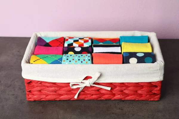 Box with colorful socks on dark table against color background