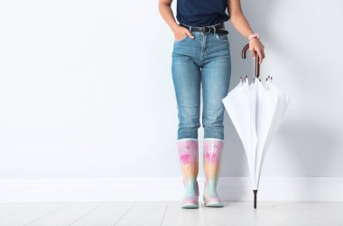 Tasarım alanı olan beyaz duvarının yakınında parlak şemsiye tutan gumboots kadında
