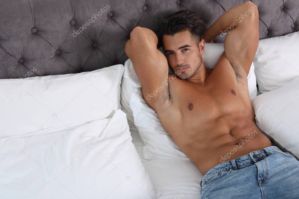 Sexy young man lying on bed with soft pillows at home