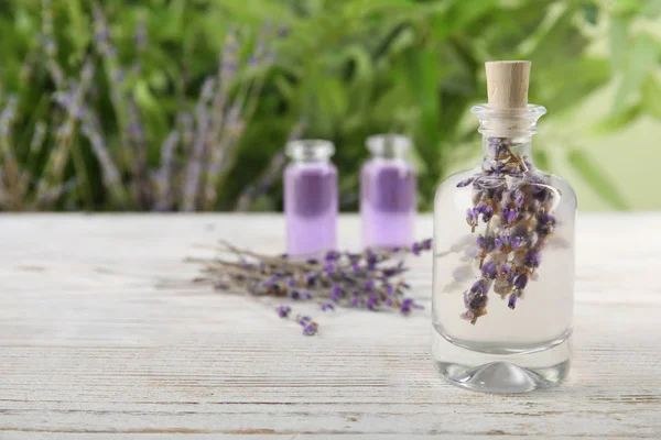 Bottle with natural herbal oil and lavender flowers on table against blurred background. Space for text