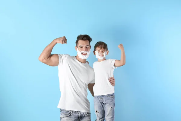 Father and son with shaving foam on faces against color background