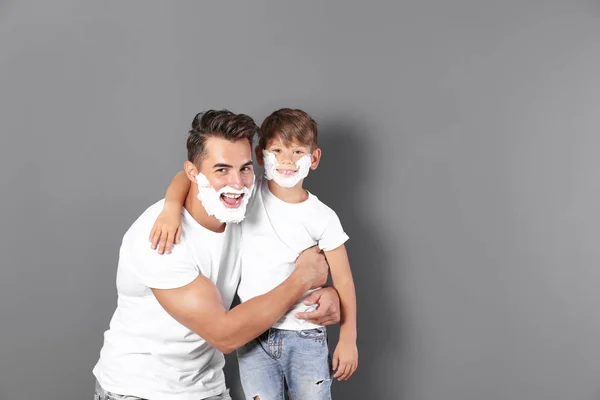 Father and son with shaving foam on faces against color background. Space for text