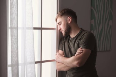 Depresyondaki genç adam evinin penceresinin yanında.