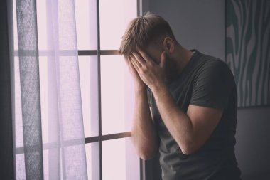 Depresyondaki genç adam evinin penceresinin yanında.