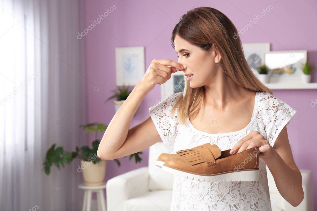 Woman spraying air freshener on shoes at home