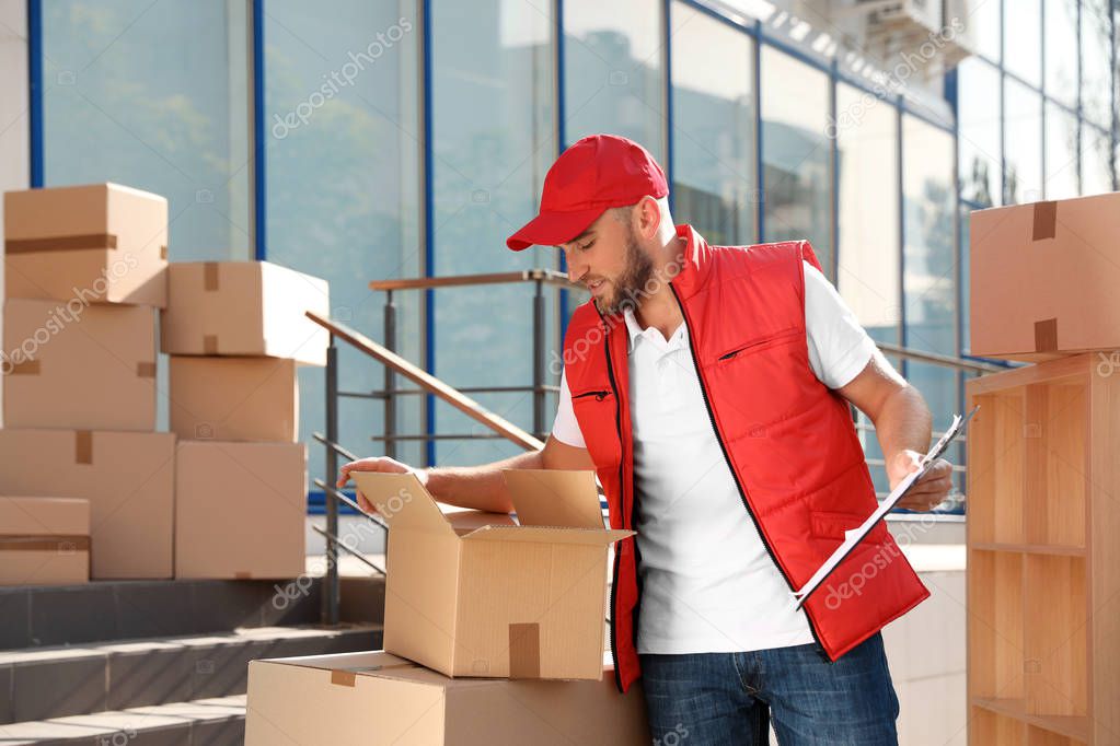Male mover with clipboard and boxes outdoors on sunny day