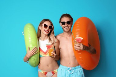Mutlu genç çift beachwear şişme yüzüklü ve renk arka plan üzerinde kokteyl