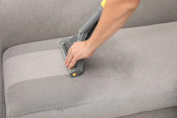Janitor removing dirt from sofa with upholstery cleaner, closeup