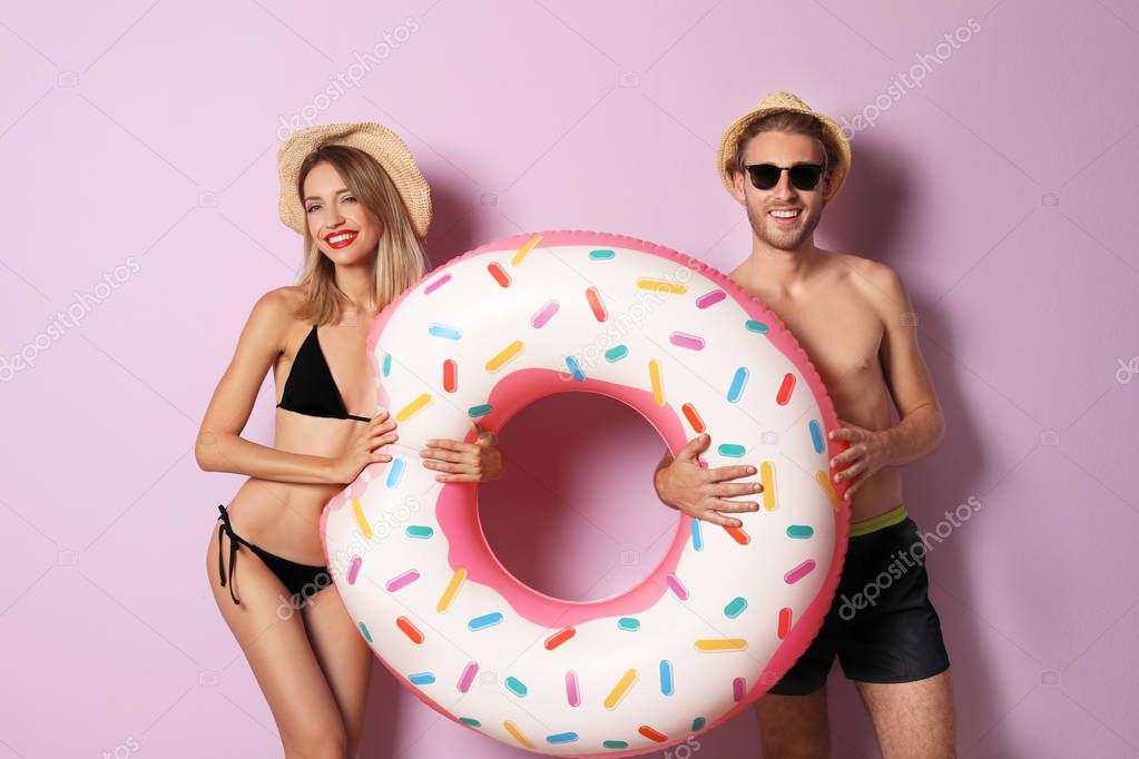 Happy young couple in beachwear with inflatable ring and cocktail on color background