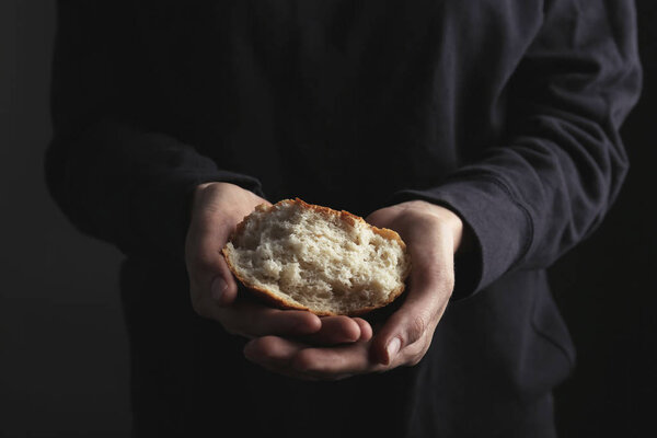 Poor woman holding piece of bread on dark background, closeup