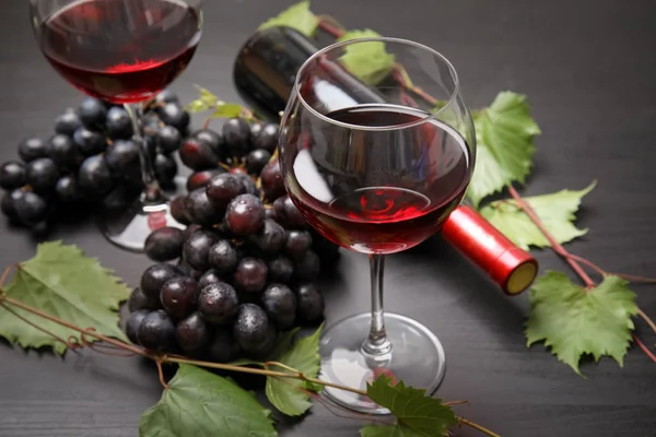 Glass and bottle of red wine and fresh ripe juicy grapes on table
