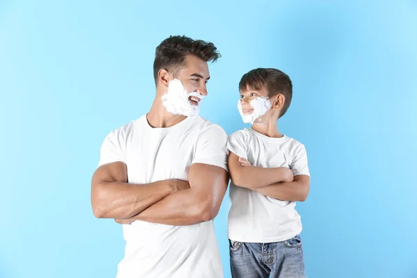 Father and son with shaving foam on faces against color background