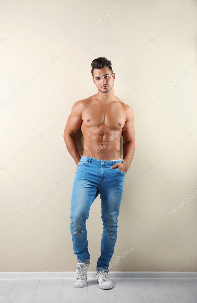 Shirtless young man in stylish jeans near light wall