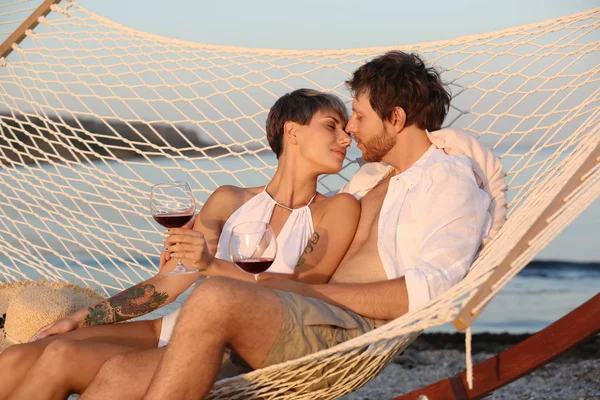 若いカップルがビーチでハンモックでワインのグラスと休憩 — ストック写真