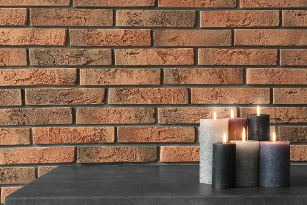 Burning candles on table against brick wall with space for text