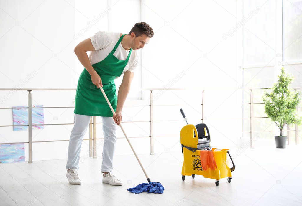 Young man with mop cleaning floor, indoors