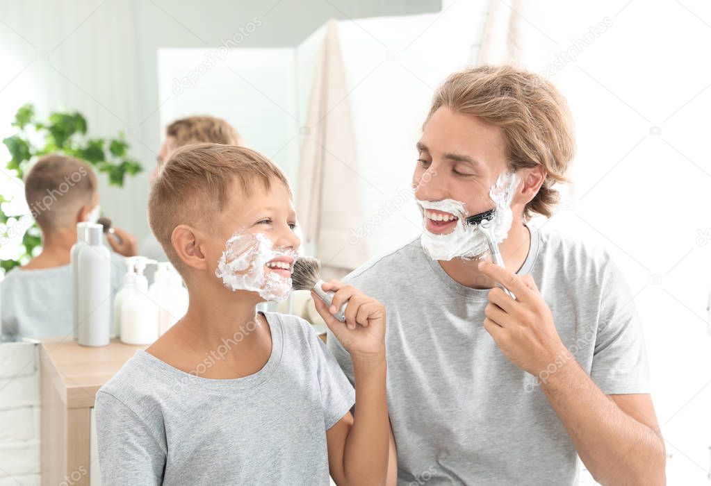 Father and son shaving together on color background