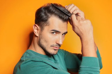 Renk arka plan üzerinde poz tarak ile genç adam. Son moda saç modeli