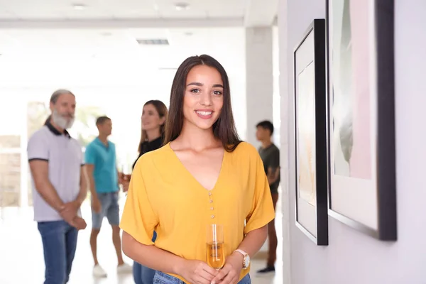 Young woman with glass of champagne at exhibition in art gallery