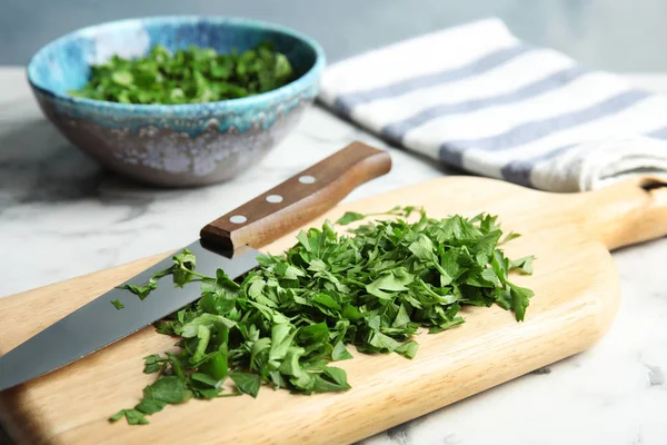 Wooden board with chopped parsley and knife on table