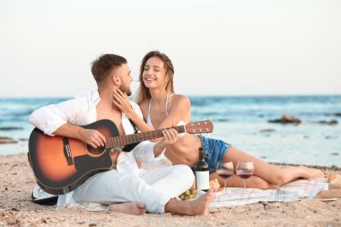 Kumsalda romantik akşam yemeği gitar ile genç çift