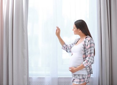 Yatağın üstüne oturan ve evde karnı dokunmadan genç güzel hamile kadın