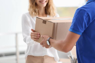 Young woman receiving parcel from courier indoors clipart