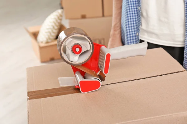 Moving box and adhesive tape dispenser indoors, closeup