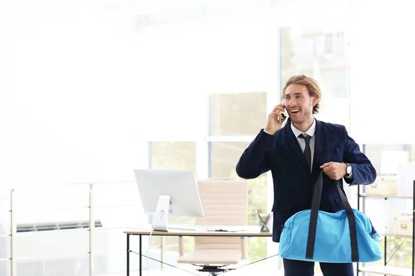 Young handsome businessman holding fitness bag in office. Space for text