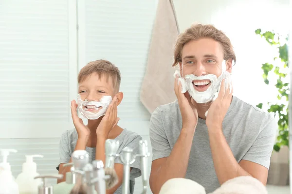 Father and son with shaving foam on faces against color background