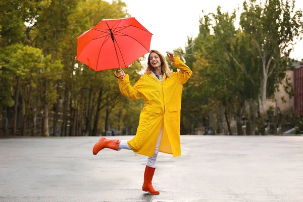 路上の黄色を身に着けている赤い傘との幸せな若い女のレインコート — ストック写真