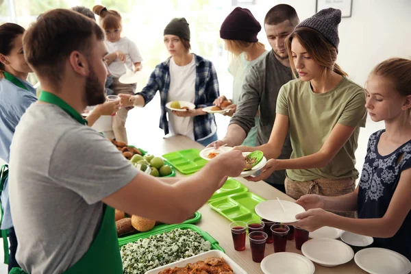 Volunteers serving food for poor people indoors