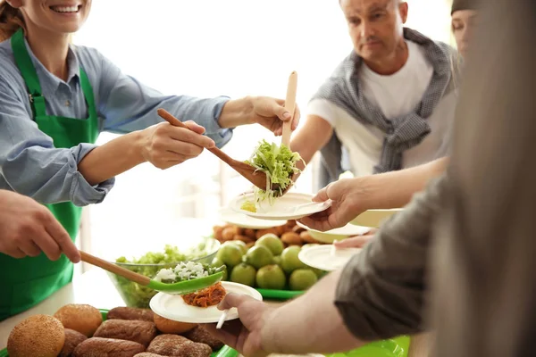 Volunteers serving food for poor people indoors