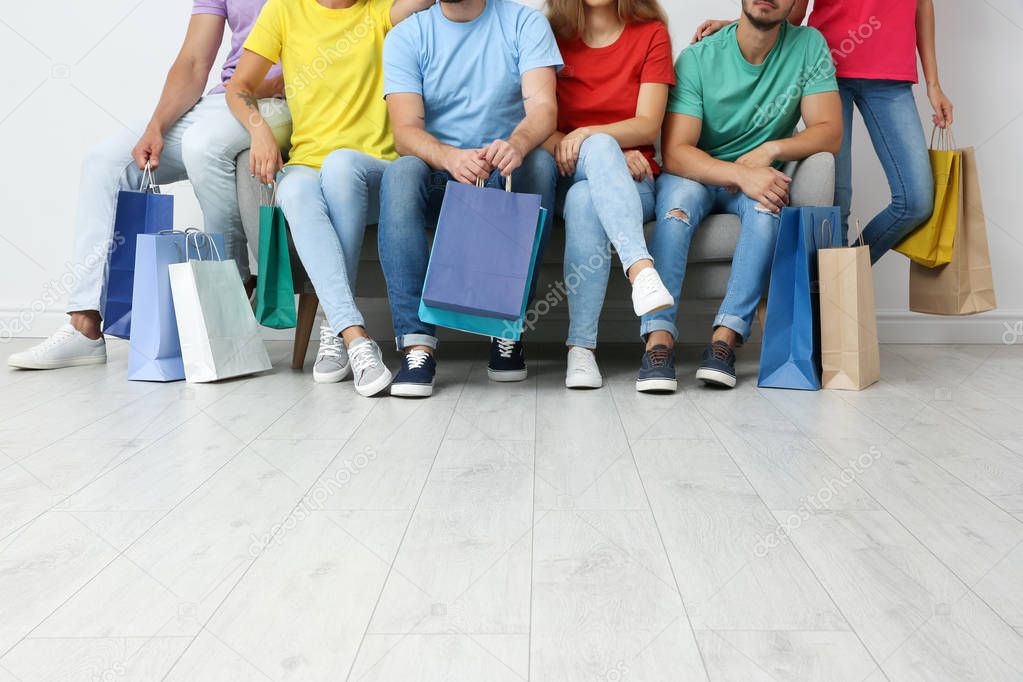 Group of young people with shopping bags sitting on sofa near light wall