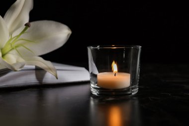 Masaya karanlıkta yanan mum, kitap ve beyaz zambak. Cenaze sembolü