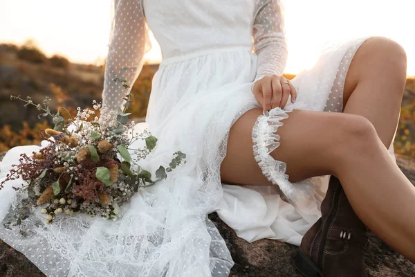 美丽的新娘与现场花束坐在岩石在日落 — 图库照片