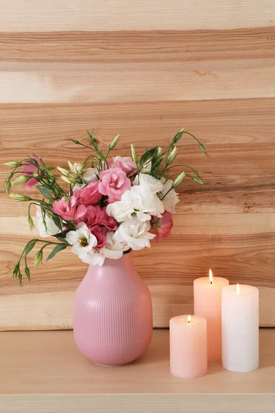 Burning candles and vase with flowers on table against wooden wall