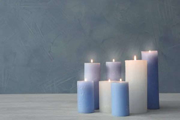 Burning candles on table against color wall with space for text